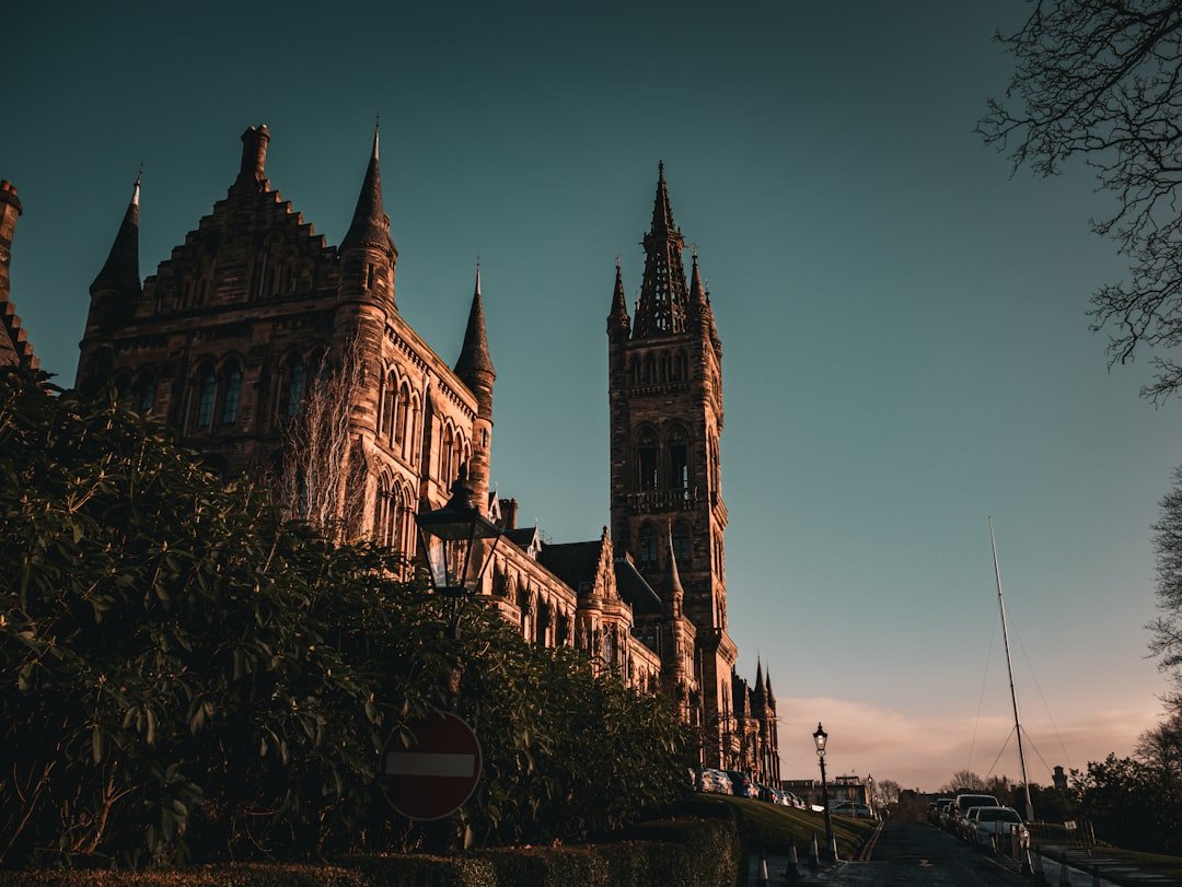 Captured at dawn, this image presents the University of Glasgow in dramatic relief, with the intricate Gothic architecture and towering spires etched against the first early light of day. The university's stonework is warmly lit by the rising sun, adding a golden hue to the historic facade.